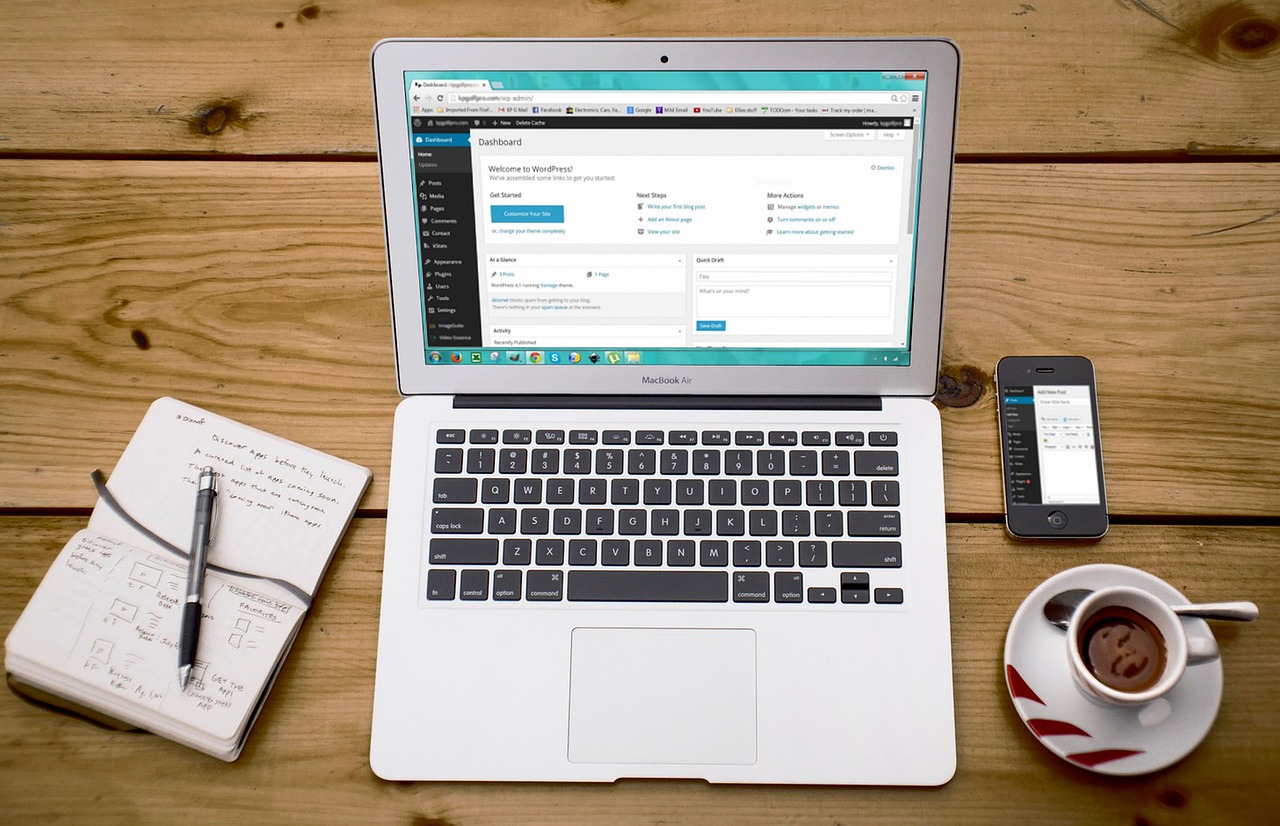 A laptop, notebook and cup of coffee on a wooden table